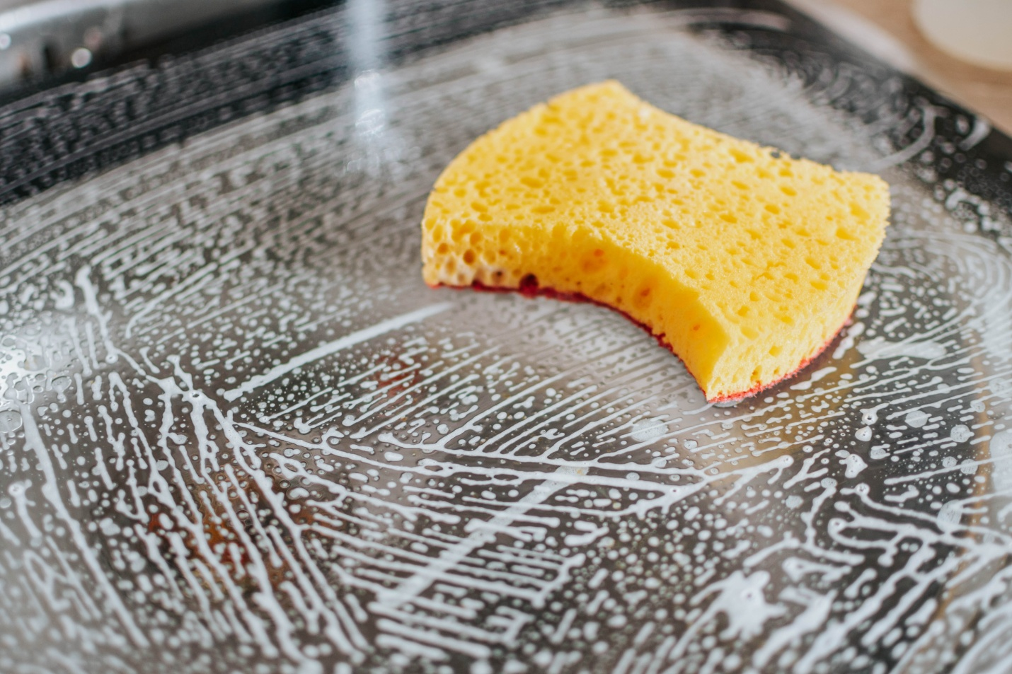 A yellow scrub on top of a soaped glass panel